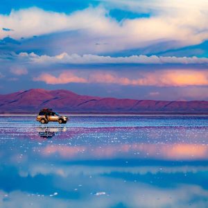 Car standing in middle of salt flat reflecting blue sky, Salar de Uyuni, Bolivia